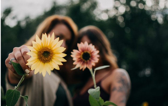 Two women smiling and holding flowers, symbolizing self-love and compassion as an Enneagram type 2.